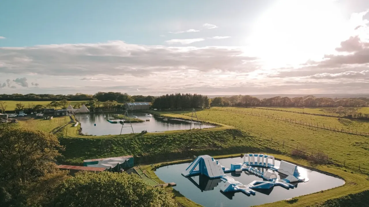 Aerial view of Wild Lakes Aqua Park in Wales featuring inflatable aqua course, surrounding lakes, green fields, and tipi tents in Narberth, Pembrokeshire.