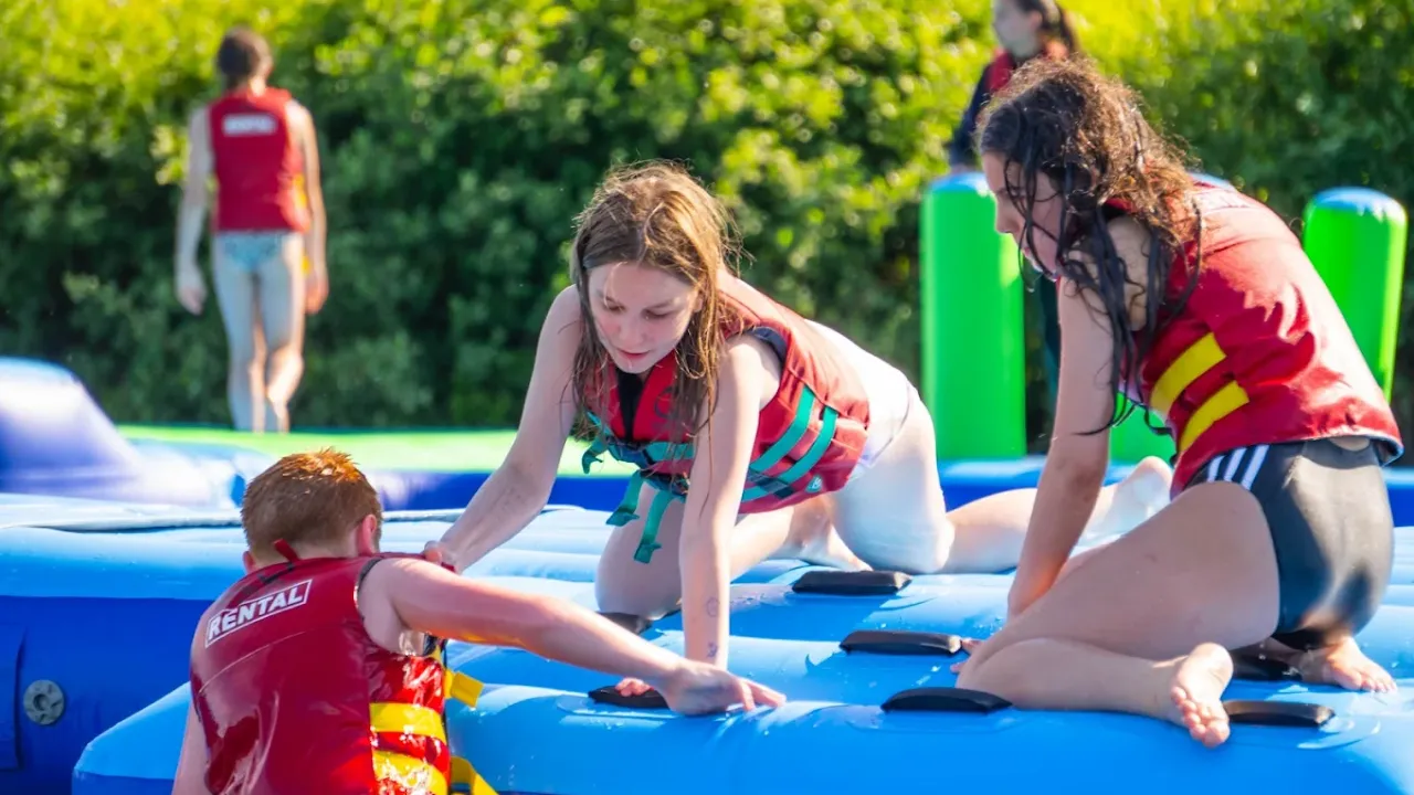 Kids in buoyancy vests climbing onto the floating Aqua Action course at Fairlop Waters.
