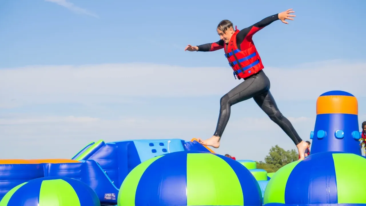 Young man mid-air jumping over inflatable balls at Aqua Action inflatable water park in Ilford, Essex.