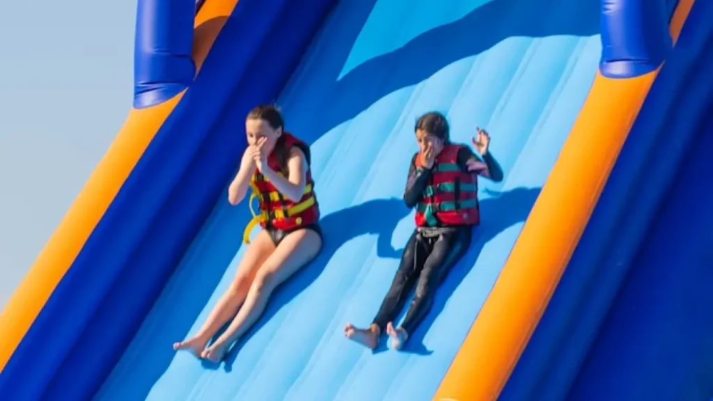 Children sliding down a large inflatable slide into the lake at Aqua Action Fairlop Waters inflatable park.