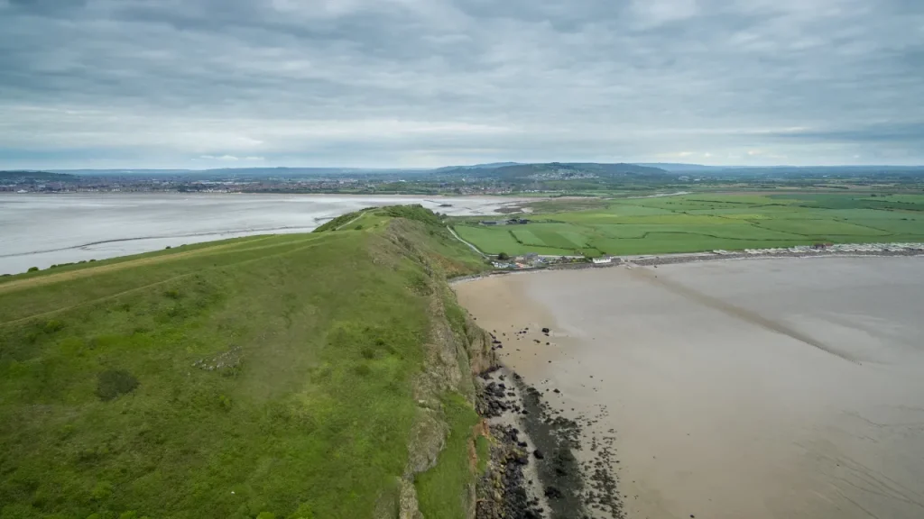 Scenic aerial view of Brean Down’s grassy headland and cliffs with Brean Beach and Weston-super-Mare visible in the distance across the Bristol Channel.