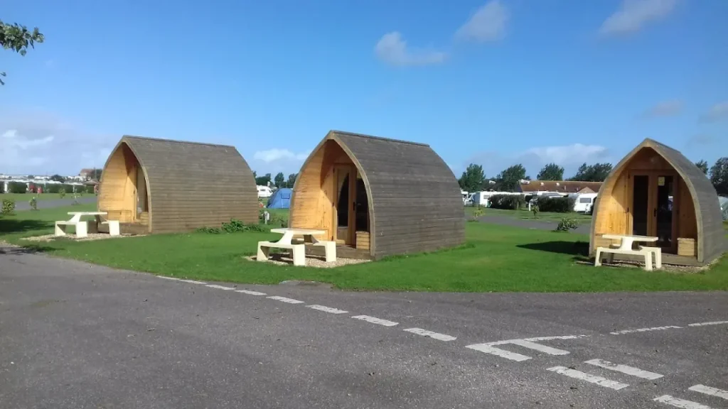 Three wooden glamping pods with picnic benches on grass pitches at Holiday Resort Unity, located near Brean Leisure Park in Somerset.