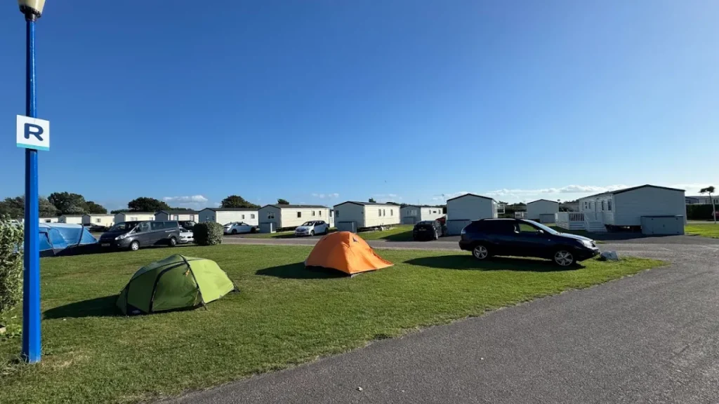 Grass touring pitches with tents, cars, and static caravans at Holiday Resort Unity near Brean Leisure Park in Somerset on a sunny day.