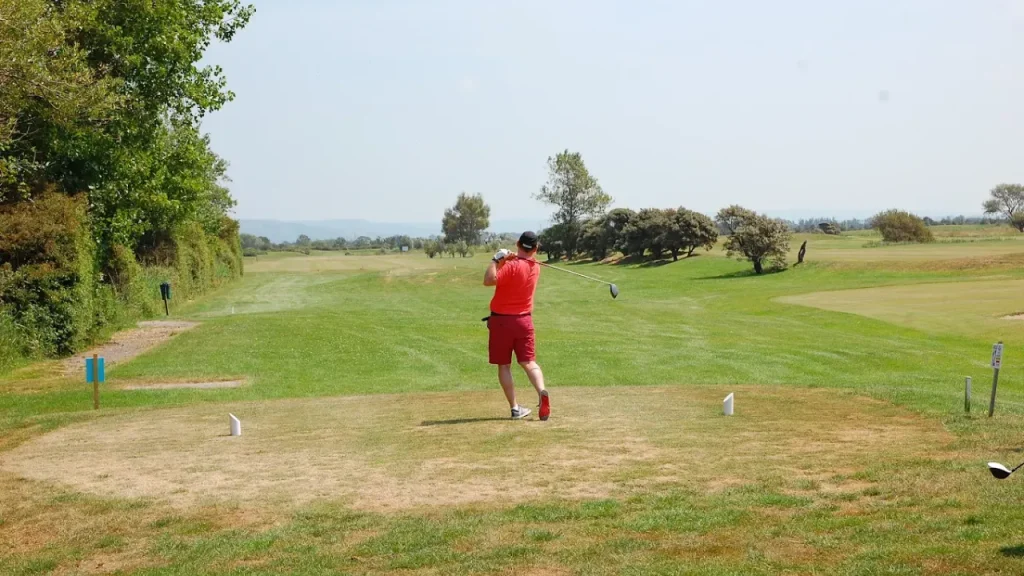 Golfer in red teeing off on a sunny fairway at Brean Golf Club, surrounded by green fields and trees near Brean Leisure Park in Somerset.