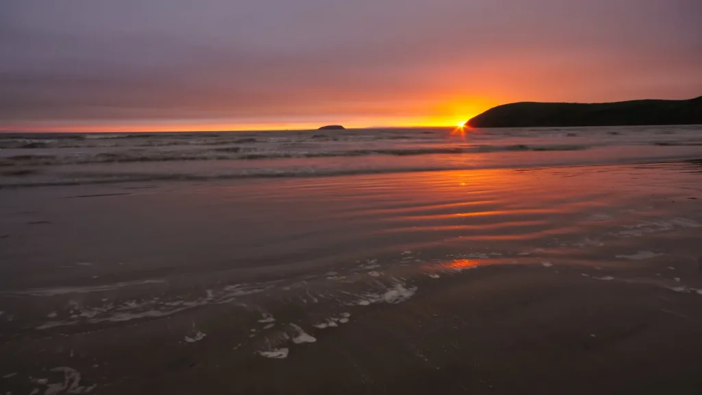 Sun setting over the sea at Brean Beach, with soft waves and golden light reflecting on wet sand beside Brean Down in Somerset.