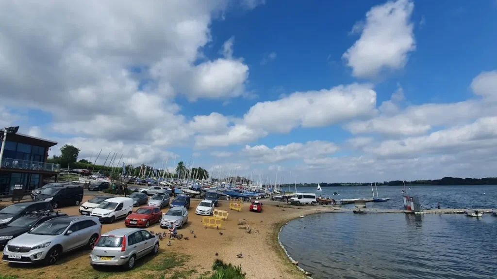 Sailing boats and parked cars at Draycote Water launch area on a sunny day.