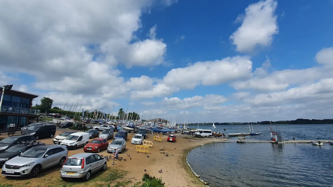 Sailing boats and parked cars at Draycote Water launch area on a sunny day.
