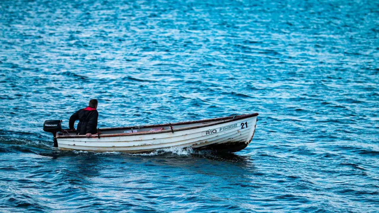 Man rowing a fishing boat on the blue waters of Draycote Water.