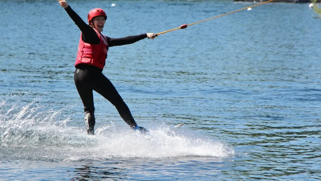 Wakeboarder smiling while riding cable tow at Liquid Leisure Aqua Park, wearing red safety gear.