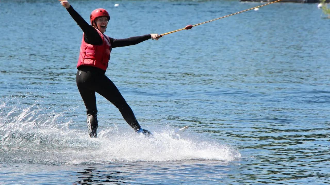 Wakeboarder smiling while riding cable tow at Liquid Leisure Aqua Park Windsor, wearing red safety gear.
