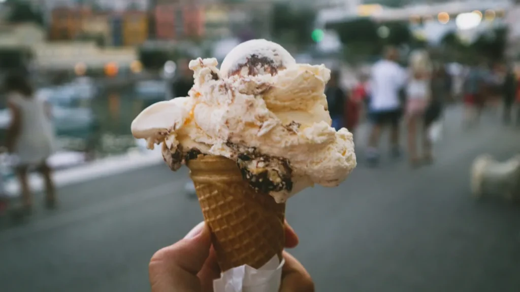 Close-up of a hand holding a large ice cream cone with chocolate and vanilla scoops at a seaside location in County Londonderry, Northern Ireland.