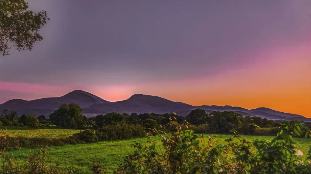 Sunset over the Mourne Mountains in Northern Ireland with Slieve Donard and Slieve Commedagh in silhouette, seen from lush countryside near County Londonderry.