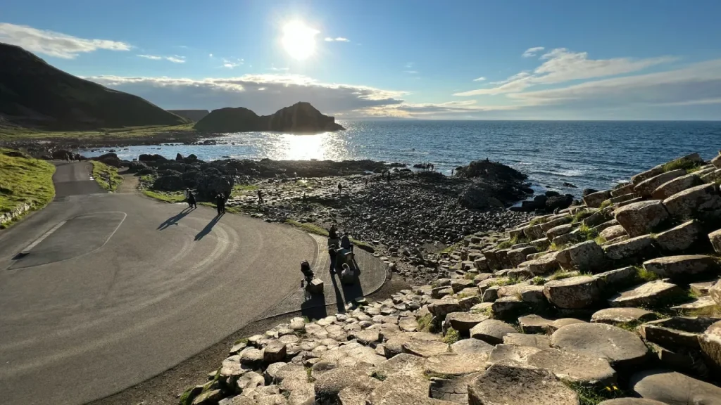 Tourists walking along the basalt columns of the Giant’s Causeway with the evening sun reflecting on the Atlantic Ocean, near County Londonderry in Northern Ireland.