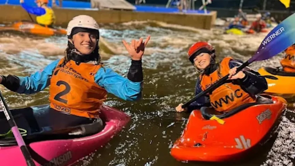 Two female kayakers smiling and posing on Pinkston’s illuminated whitewater kayaking course in Glasgow.