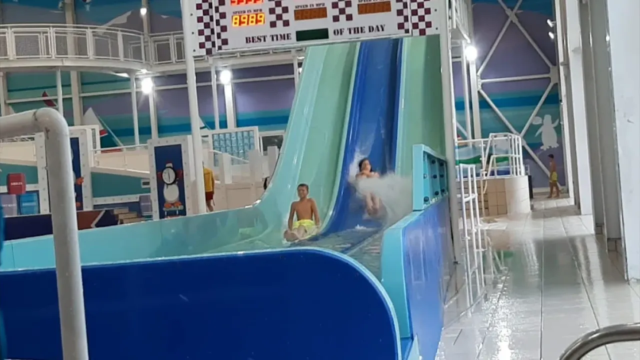 Children sliding down twin flumes at Splashaway Bay water park, with splash at bottom and speed timer above.
