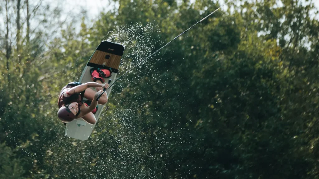 Wakeboarder wearing helmet and life vest performing an aerial flip over the water at Thorpe Lakes Aqua Park’s cable course.