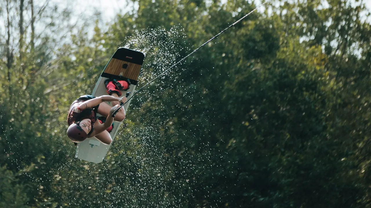 Wakeboarder wearing helmet and life vest performing an aerial flip over the water at Thorpe Lakes Aqua Park’s cable course.