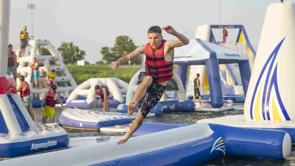 Teenager jumping between inflatable platforms at Thorpe Lakes Aqua Park’s obstacle course, with others climbing in the background.