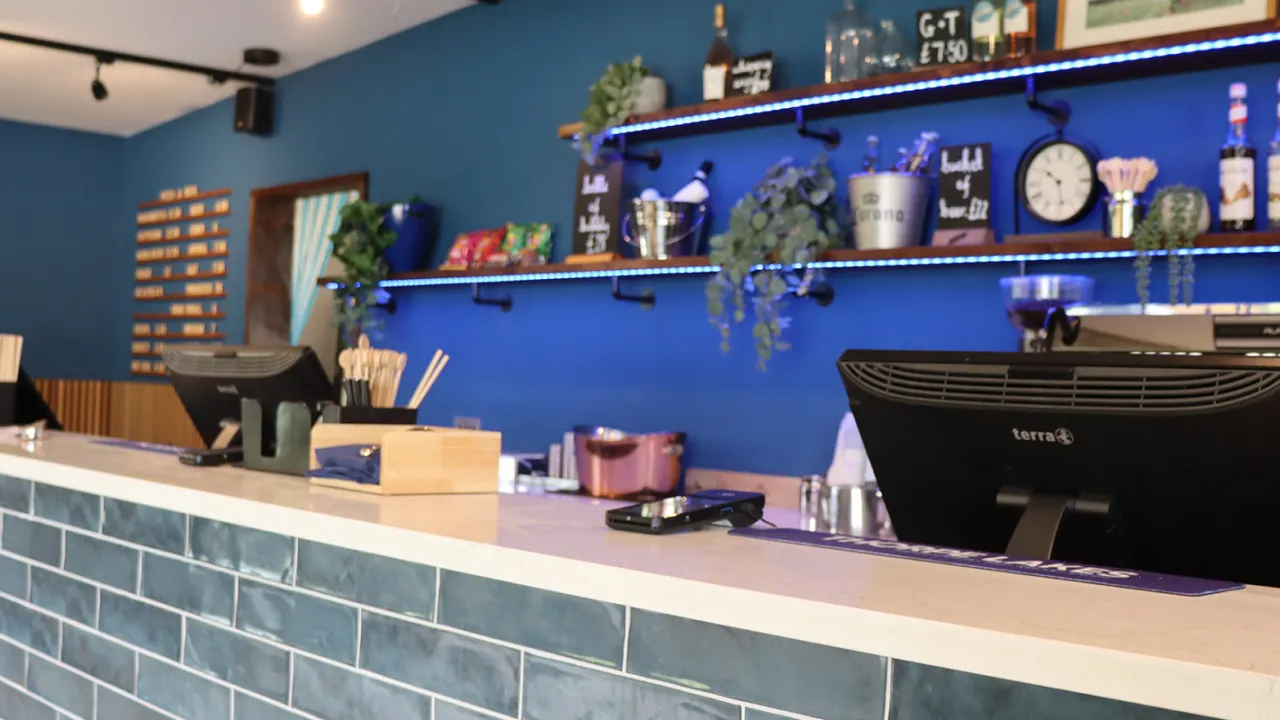 Contemporary café counter at Thorpe Lakes Aqua Park with shelves displaying snacks, drinks, and bar essentials against a stylish blue wall.