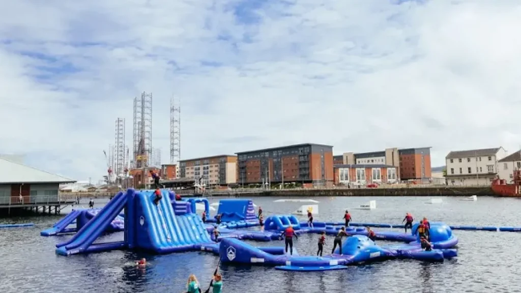 Inflatable aqua park at Wild Shore Dundee with visitors climbing and playing on blue obstacles in City Quay.