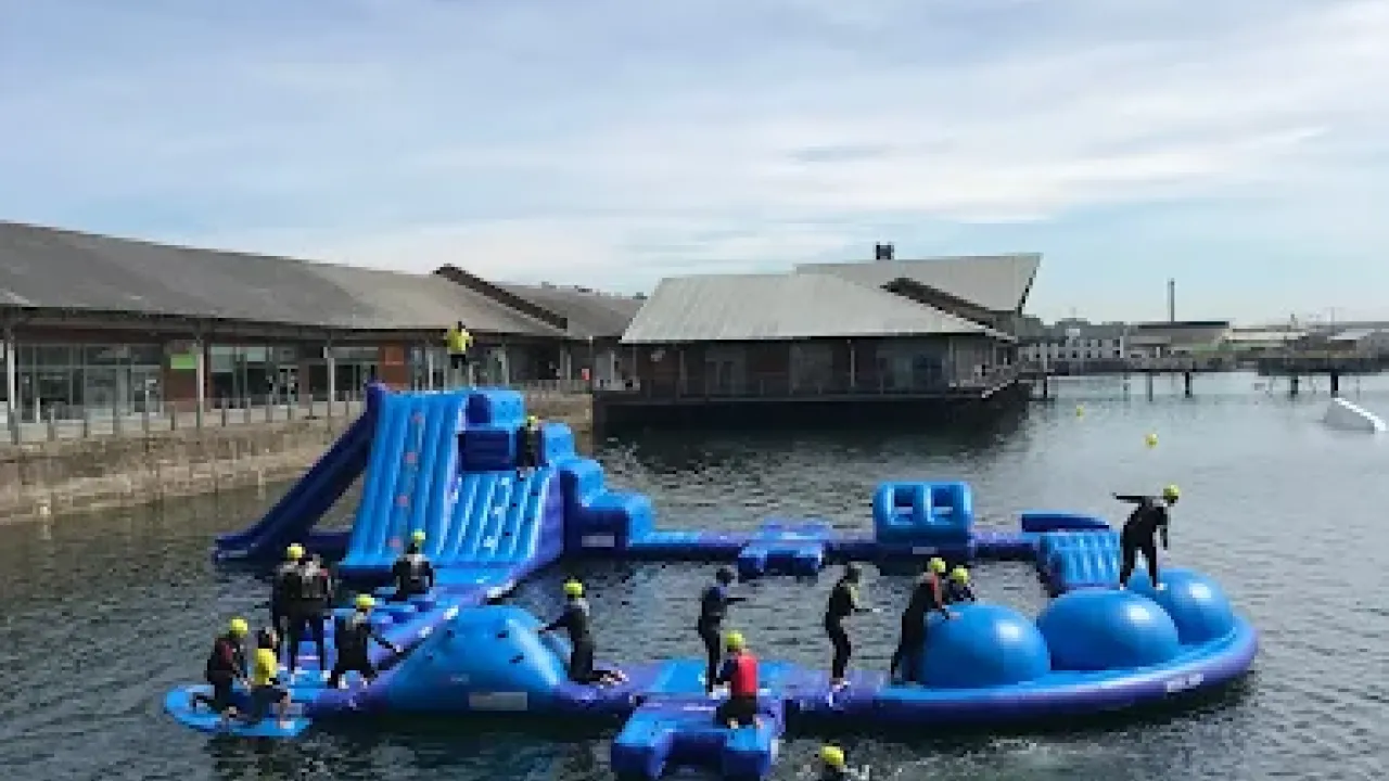 Visitors navigating a floating obstacle course at Wild Shore Dundee in front of City Quay buildings.