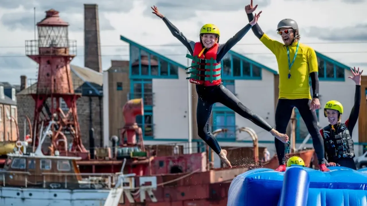 Girl in wetsuit jumping from inflatable with instructor cheering at Wild Shore Dundee.
