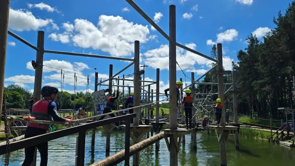 Visitors navigating the elevated obstacle course at Foxfall, Foxlake Adventures, wearing safety harnesses and helmets above water platforms.