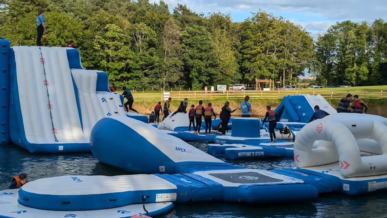 People enjoying the inflatable Aqua Park course at Foxlake Adventures, featuring slides, trampolines, climbing walls, and floating walkways.