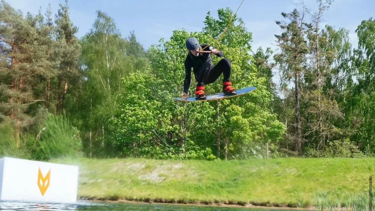 Wakeboarder performing an aerial trick at Foxlake Adventures, wearing safety gear and using the cable tow system on the lake.