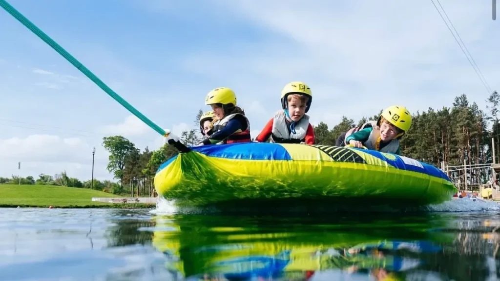 Group of children wearing helmets and life vests riding an inflatable ringo on the water at Foxlake Adventures in East Lothian.