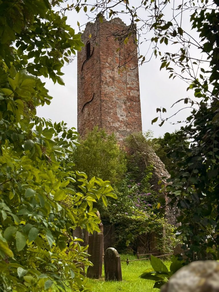 The old church tower in Ballymoney, Northern Ireland, dating back to 1637, surrounded by greenery and historic gravestones.