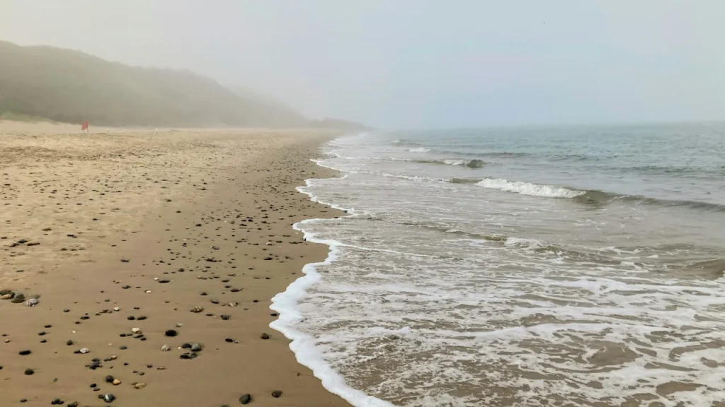 Misty morning at Whiterocks Beach near Ballymoney, Northern Ireland, with gentle waves and pebbles scattered along the sandy shoreline.