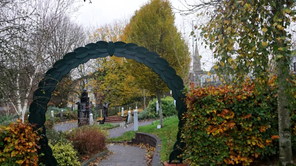 Pathway through the Joey and Robert Dunlop Memorial Garden in Ballymoney, Northern Ireland, with archway and seasonal foliage.