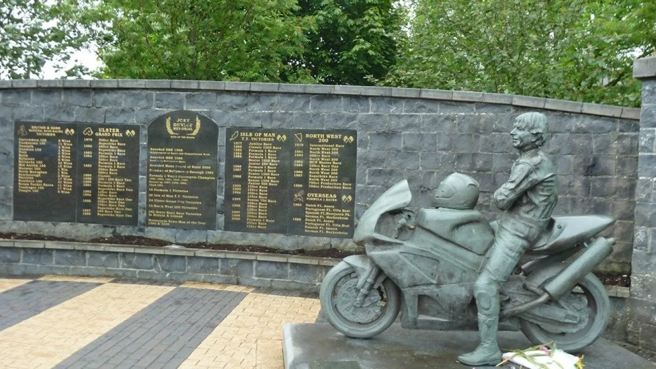 Statue of Joey Dunlop beside his motorbike at the Joey and Robert Dunlop Memorial Garden in Ballymoney, Northern Ireland, with engraved plaques of racing achievements.