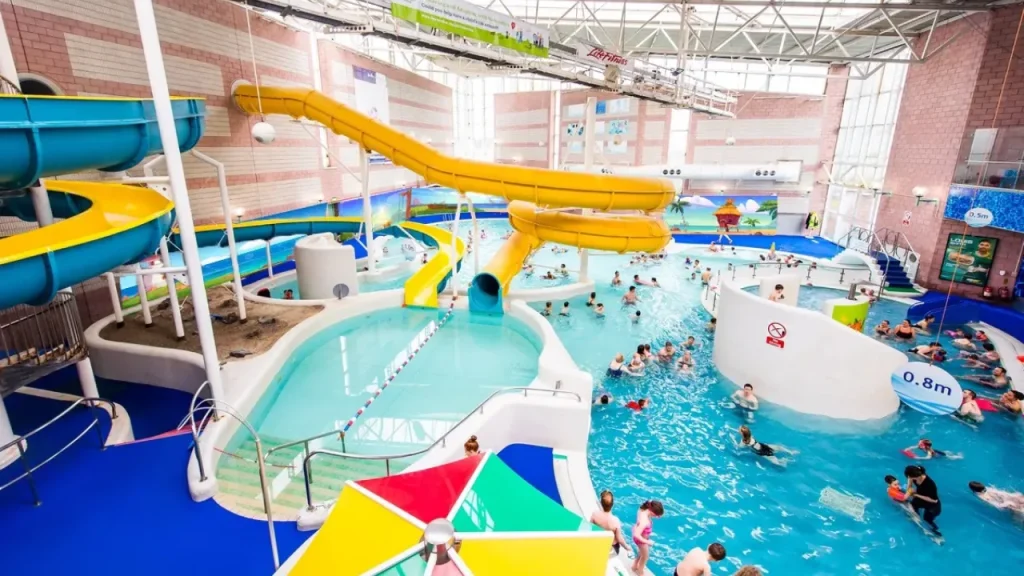 Interior view of Perth leisure pool showing yellow water slides, large indoor swimming pool with families, multiple pool levels, brick architecture, and recreational water features in Scotland's premier water leisure centre