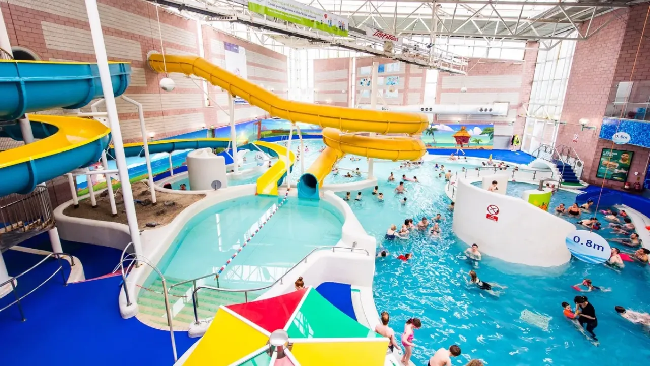 Interior view of Perth leisure pool showing yellow water slides, large indoor swimming pool with families, multiple pool levels, brick architecture, and recreational water features in Scotland's premier water leisure centre