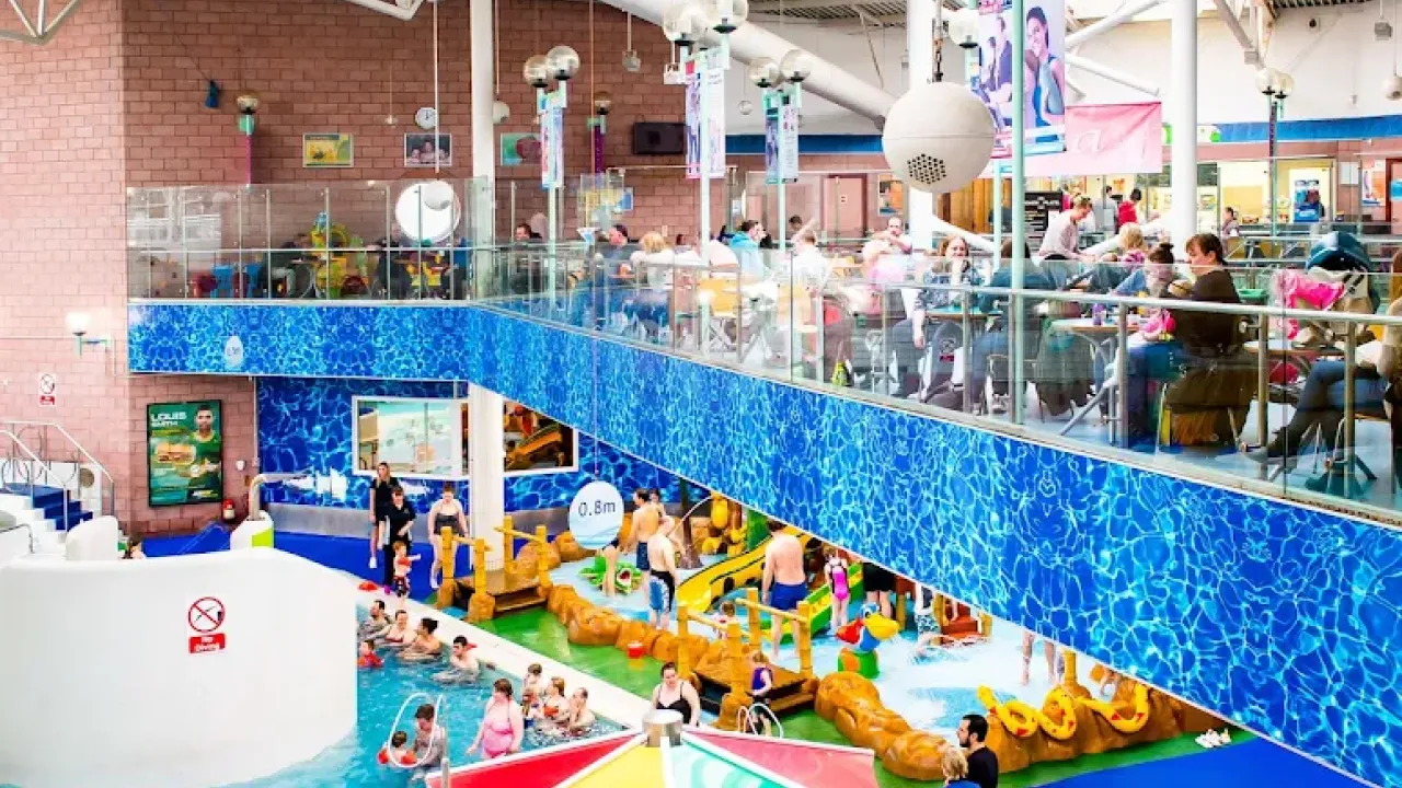 Perth leisure pool interior showing the Monkey Jungle children's play structure with orange pirate ship design, main swimming pool with blue water, spectator viewing areas, and families enjoying the water attractions