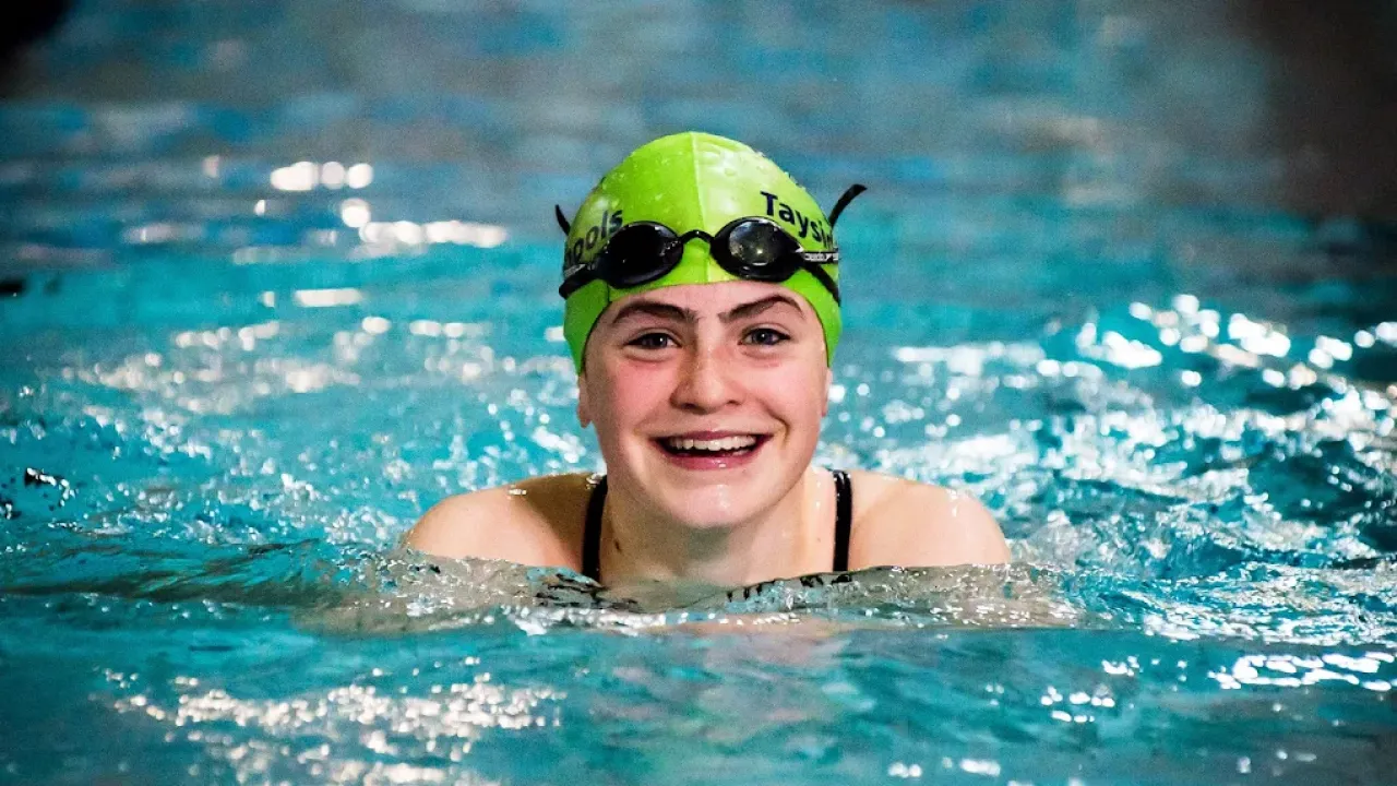 Smiling young female swimmer wearing green swim cap and goggles in Perth leisure pool's clear blue training water, showcasing the facility's competitive swimming programmes