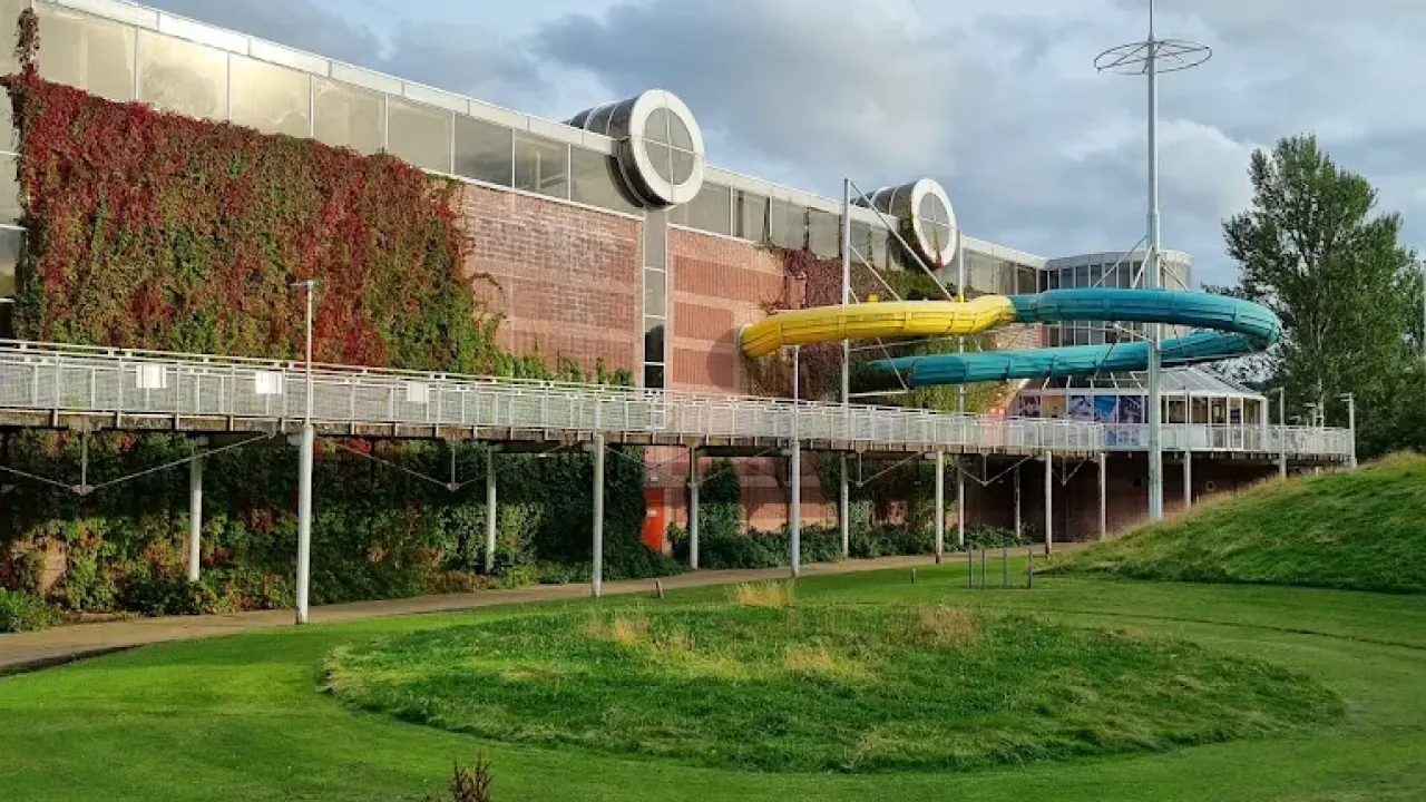 Exterior view of Perth leisure pool showing yellow and green water slide sections extending outside the brick building, ivy-covered walls, elevated walkways, and landscaped grounds in Perth Scotland