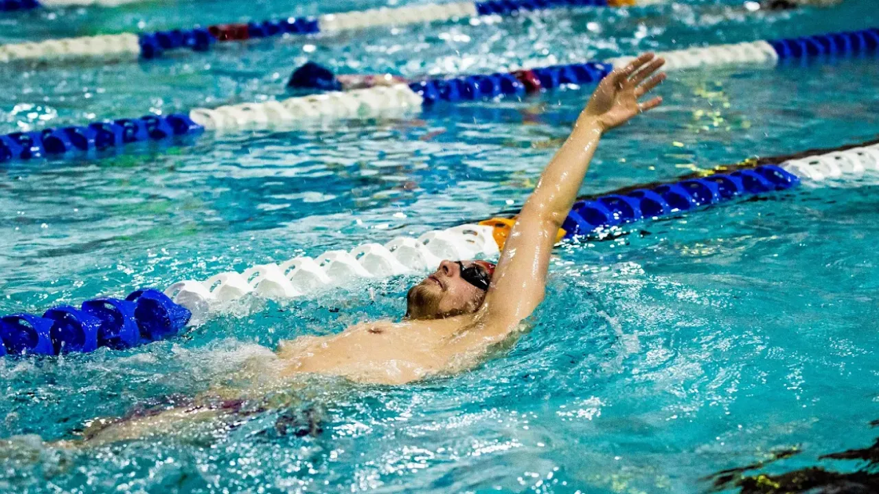 Competitive swimmer performing backstroke technique in Perth leisure pool's lane swimming area with blue lane ropes and clear training water, showcasing the facility's professional swimming environment