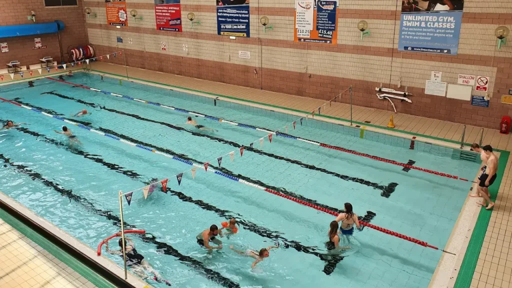 Multiple swimmers training in Perth leisure pool's lane swimming facility with clear lane ropes, promotional banners advertising gym and pool packages, and brick architecture showing the professional training environment
