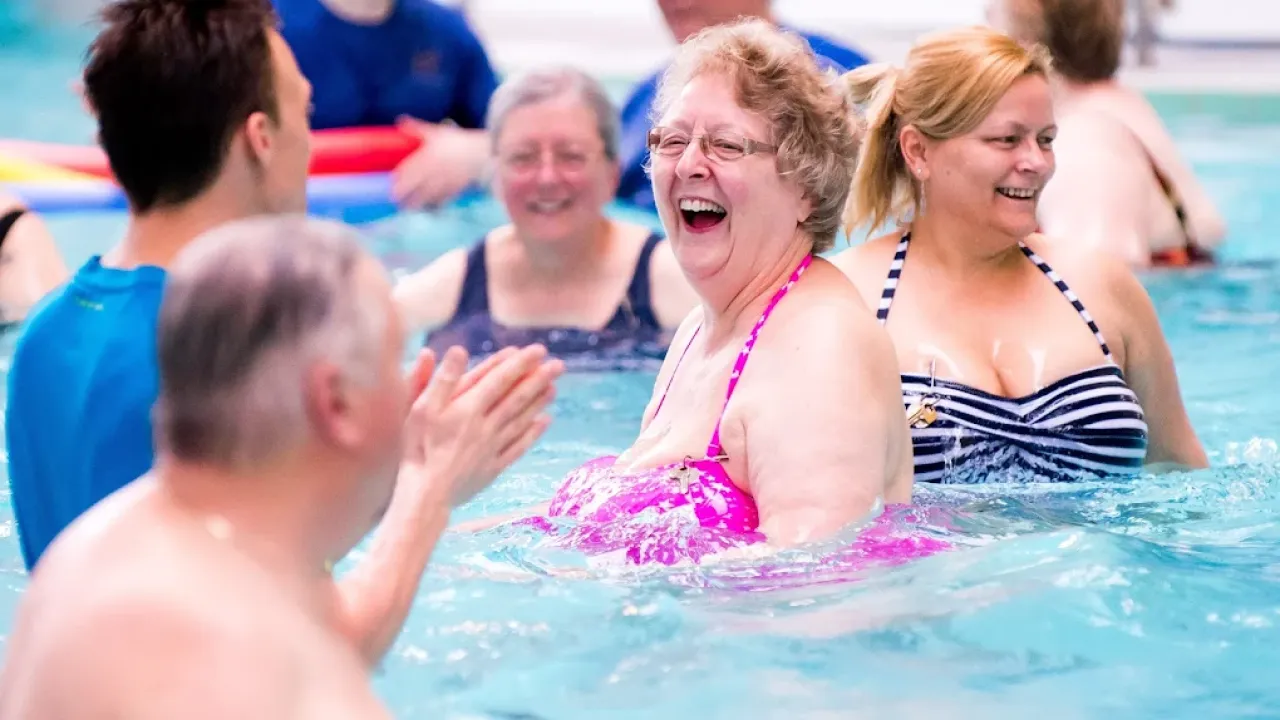 Group of happy adults participating in aqua fitness class at Perth leisure pool, with instructor leading exercise in clear blue water, showing the social and enjoyable nature of adult swimming programmes