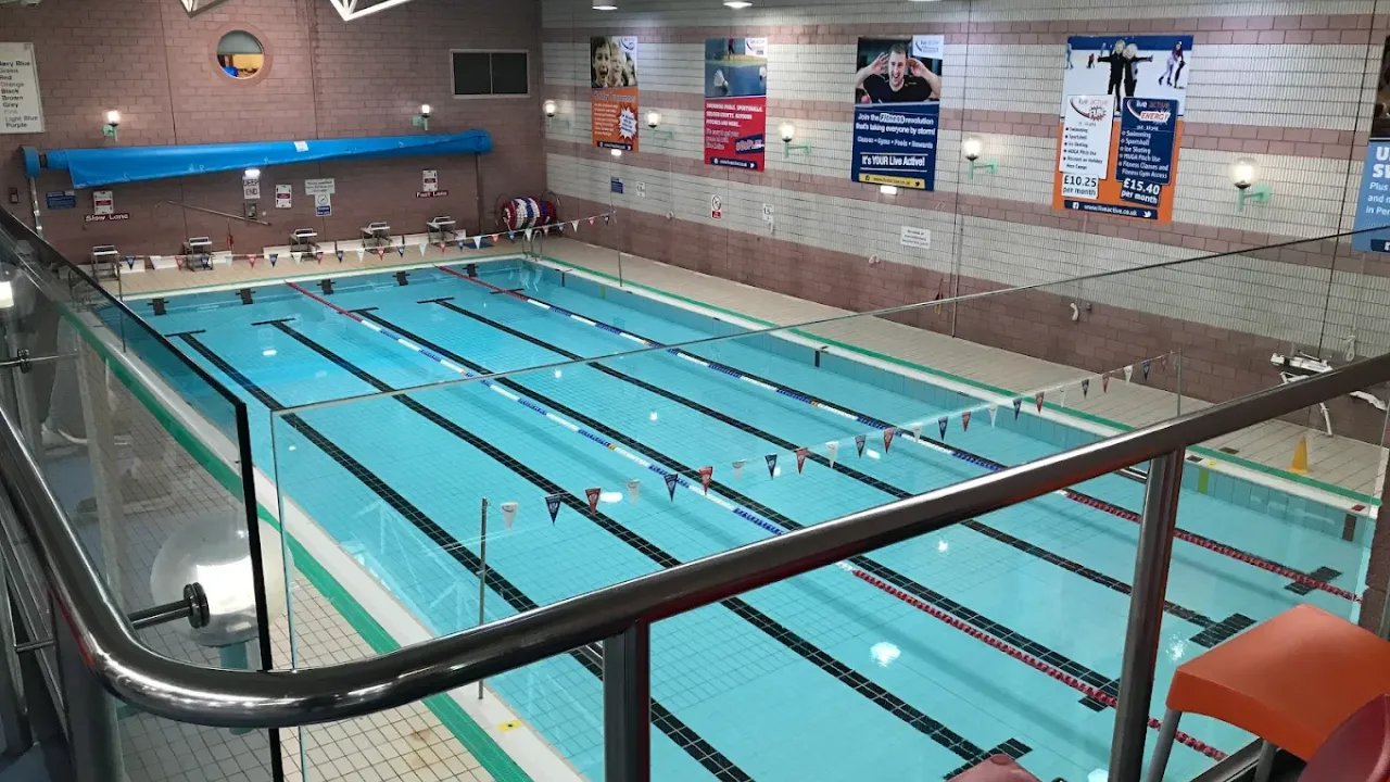 Perth leisure pool training facility showing multiple swimming lanes with lane ropes, clear blue water, brick architecture, spectator viewing area, and promotional posters on walls