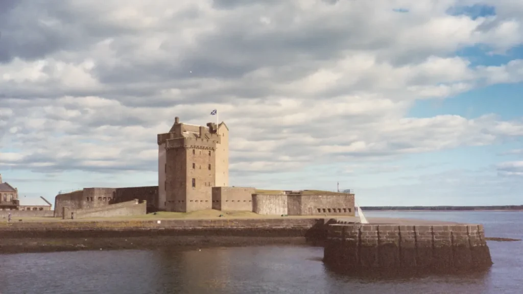 Broughty Castle on the Dundee waterfront, with a stone fort and tower beside the water under a cloudy sky, and a Scottish flag flying.