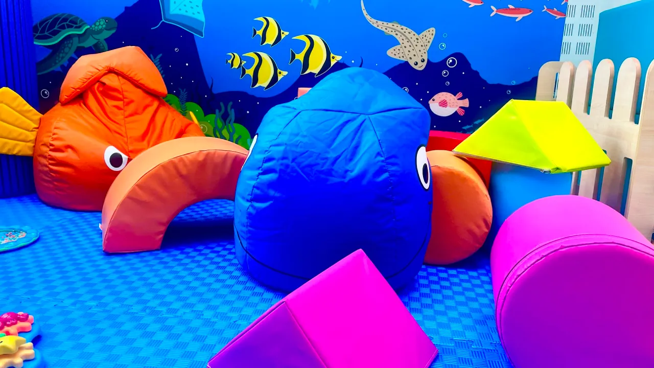 Colourful soft-play area with blue and orange fish-shaped beanbags, foam shapes, and an underwater sea-life mural at Dundee Olympia Leisure Pool, Dundee.