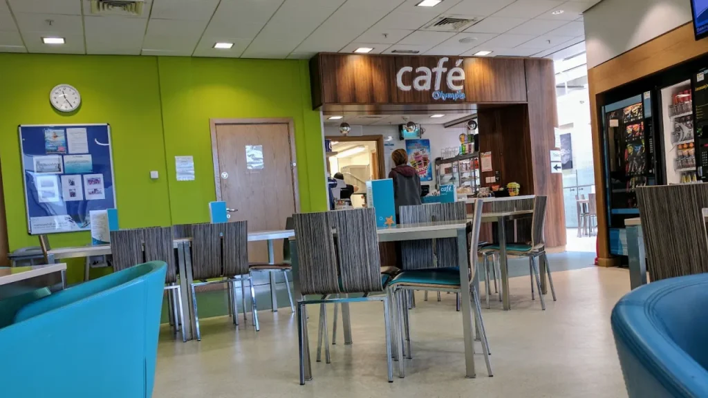Seating area in front of Café Olympia at Dundee Olympia Leisure Pool, with tables, chairs, a green wall, and the café counter in the background.