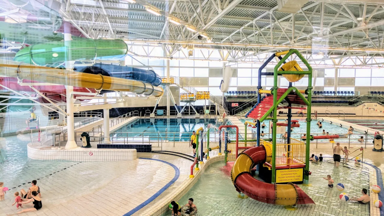 Wide view of Dundee Olympia Leisure Pool showing the indoor leisure pool, colourful flume slides, and a children’s water play structure with tipping bucket and shallow splash area.