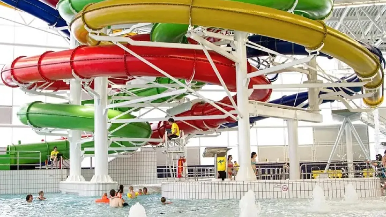 Close-up of Dundee Olympia Leisure Pool flume slides in red, green, yellow, and blue, with swimmers in the pool and a lifeguard on duty.