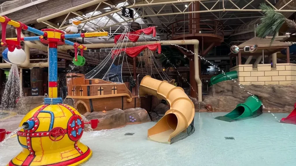 Pirate-themed indoor splash area at Sandcastle Waterpark in Blackpool, with a ship play structure, water jets, shallow pool, and small yellow and green slides.