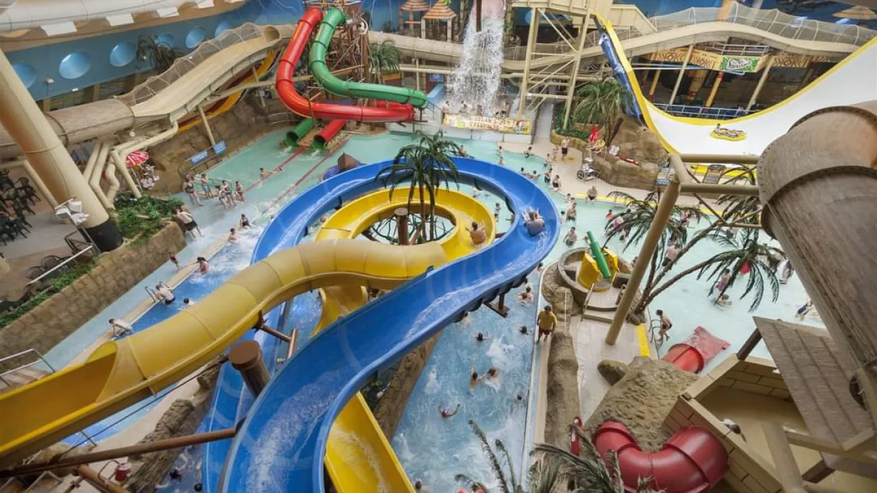 Overhead view inside Sandcastle Waterpark in Blackpool showing twisting blue and yellow flumes, a lazy-river style channel, palm trees, and multiple indoor slides with swimmers.